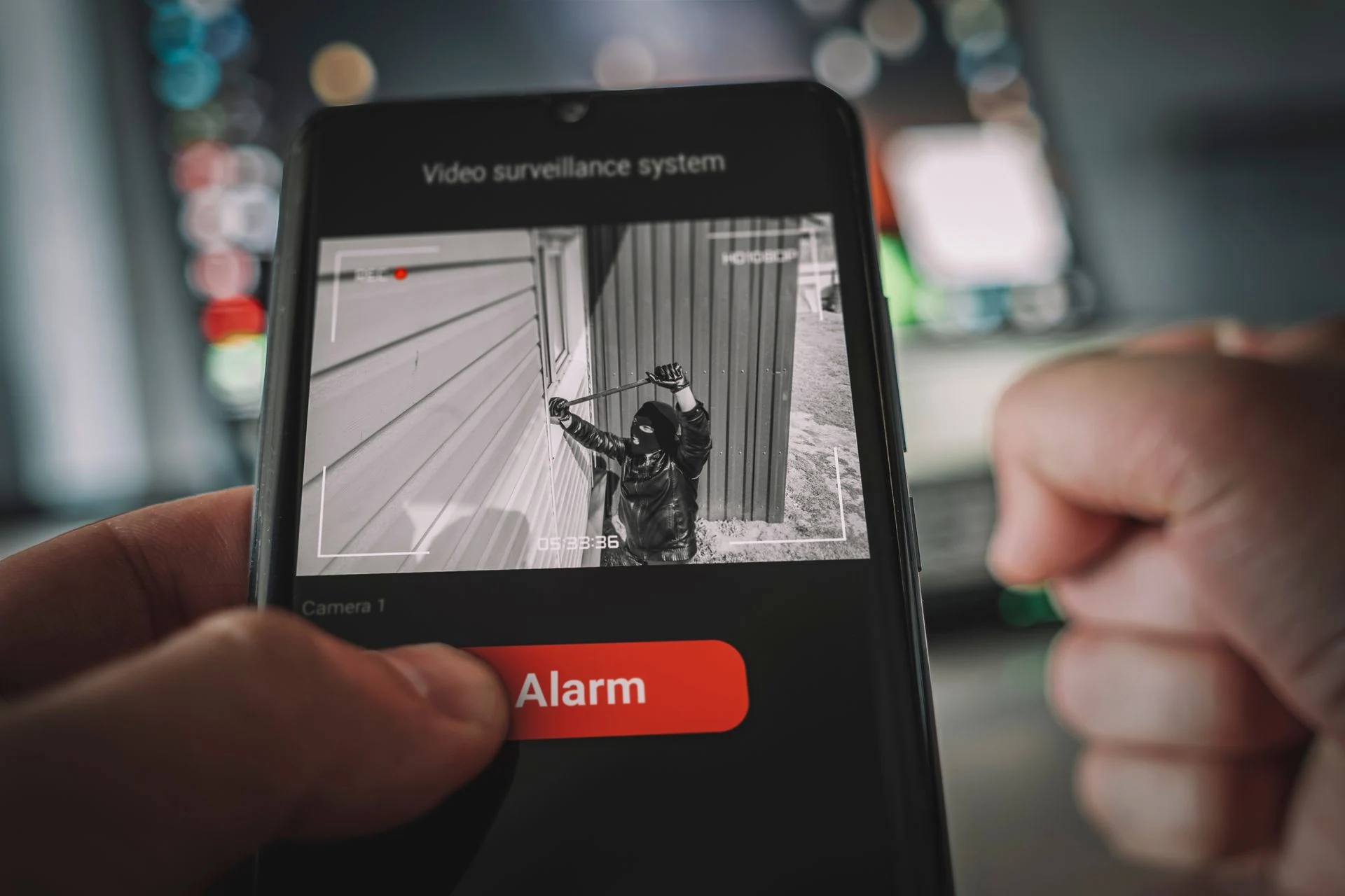 Security app on a smartphone showing a camera view of an intruder and an alarm button